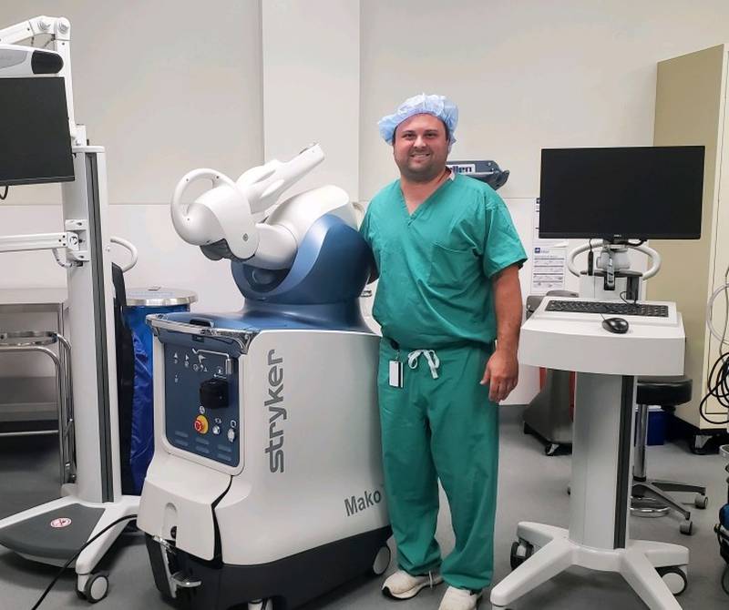 OSF's Connor Kasik, DO, orthopedic surgeon, stands with the robotic-arm assisted joint replacement, Stryker Mako SmartRobotics system.