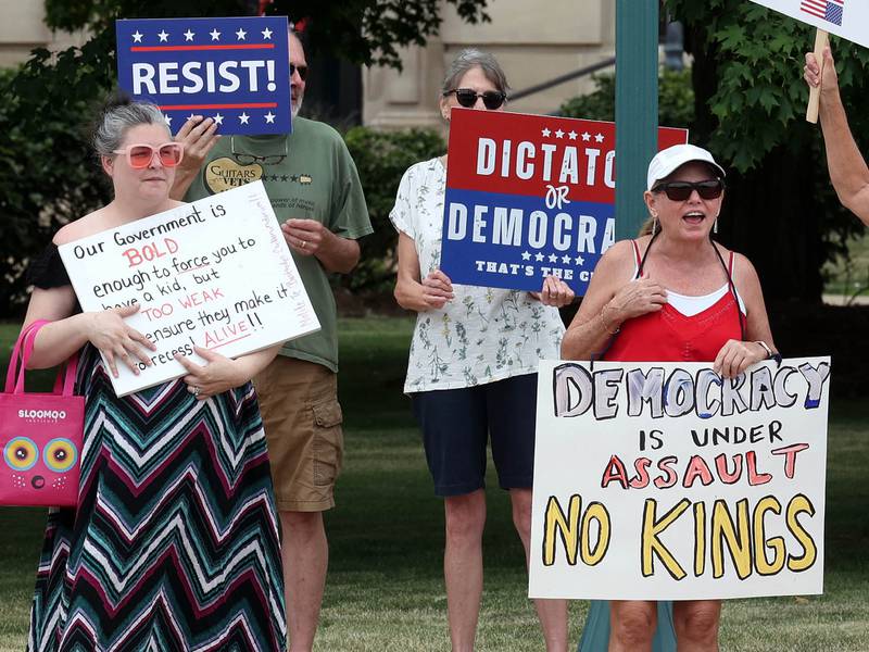 Protesters hold signs and ring bells Saturday, July 4, 2025, at the corner of Main and State Streets in front of the DeKalb County Courthouse in Sycamore for a "No Kings" rally to voice their displeasure with President Donald Trump.
