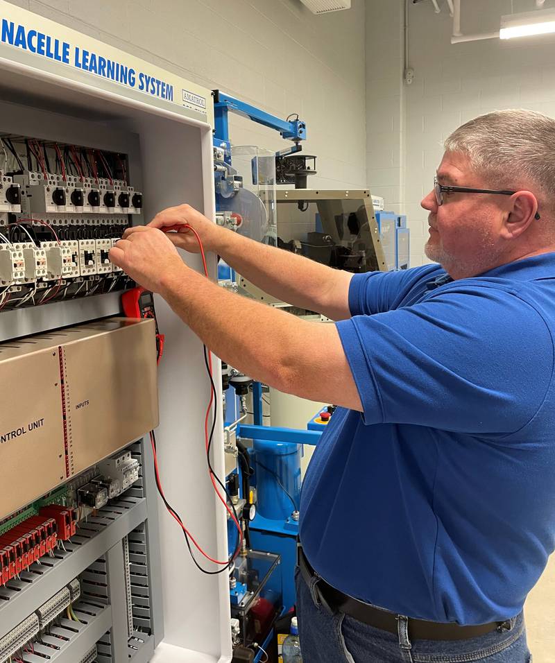 Wind technology instructor Steve Malavolti uses a multimeter to check a circuit on a Turbine Control Unit in Illinois Valley Community College's wind lab.