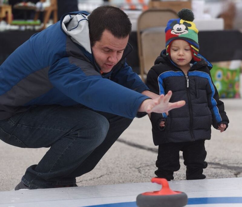 Chris Lalla of Oak Brook demonstrates curling for his son, Mason, 1, during Frozen Fest Saturday in Glen Ellyn. (Joe Lewnard | Staff Photographer)