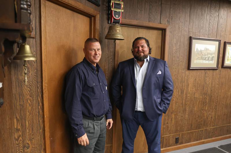 Rovanco Piping Systems business partners and cousins, Todd Stonitsch, left, and Chad Godeaux pose for a photo under the Brugg bell which is rung whenever there is a million dollar sell.