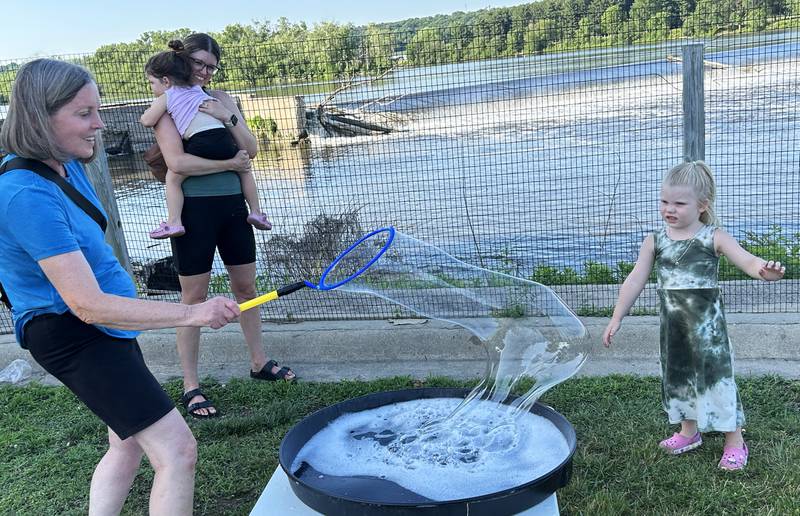 Avery Hoen, 4, of Naperville, waits to pop a big bubble made by her grandma, Chris Donahue, of Oregon, at the River's Edge Farmers Market in Oregon on Thursday, June 19, 2025. The bubble fun was provided by "Bubble Guy" Jason Kollom, who was sponsored by the Oregon Public Library.. The Farmers Market is held Thursday nights 5-7:30 p.m. at 123 N. 2nd St., in Oregon.