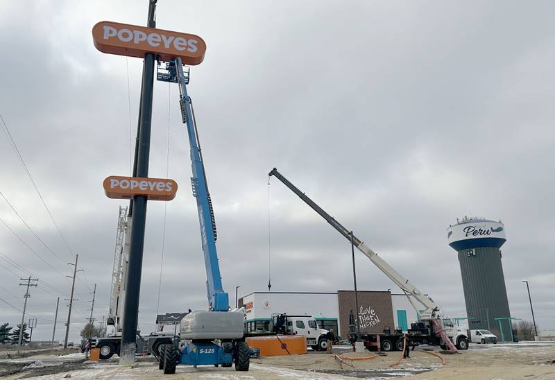 Crews hoist Popeyes signs in place for the new location near the intersection of May Road and Trompeter Road on Tuesday, Dec. 3, 2024 in Peru.