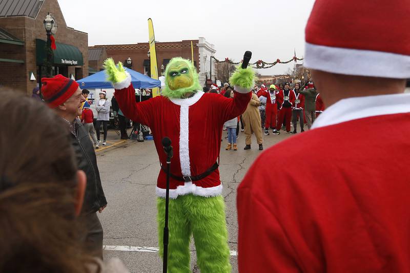 Russ Hyatt of Sundowner Entertainment, dressed as the Grinch tries to direct the Voices In Harmony choir before they sing the “National Anthem” before the start of the McHenry County Santa Run For Kids Sunday morning, Dec. 3, 2023, in Downtown Crystal Lake. The annual event raises money for agencies in our county who work with children in need.