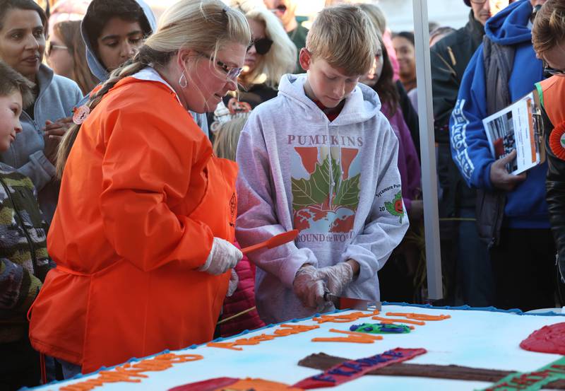 This year’s Pumpkin Festival Theme Contest winner Sam Schwartz, 10, a fifth grader from North Grove Elementary School in Sycamore, cuts the first piece of cake as Brandi Voigt, theme director of the Pumpkin Fest Committee, looks on Wednesday, Oct. 23, 2024, on North Maple Street adjacent to the DeKalb County Courthouse during the Sycamore Pumpkin Festival.