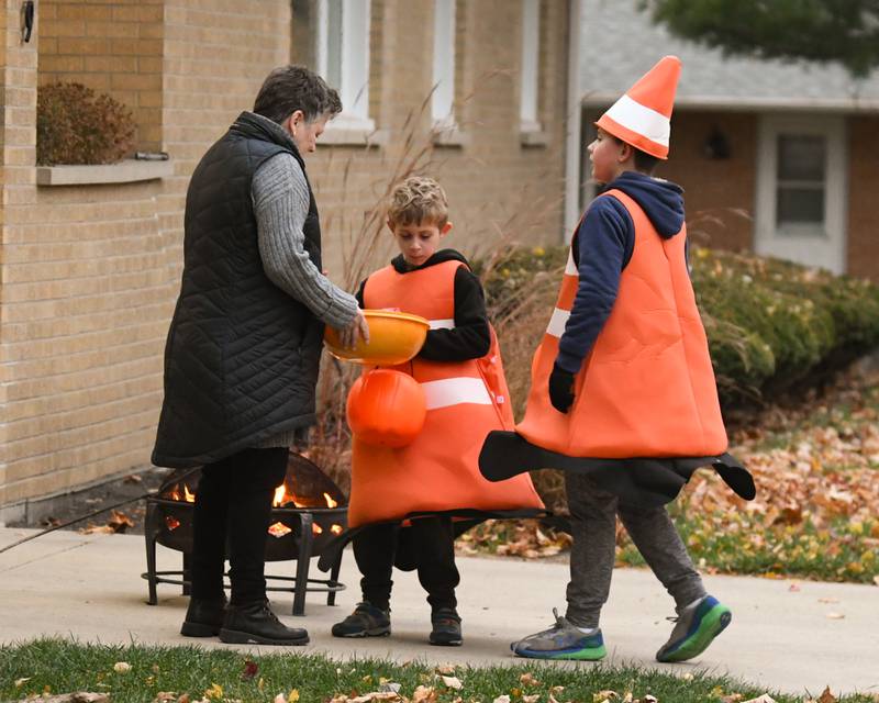 Cathy Ecker hands out candy to Peyton Harper, 10, and his brother Sebastian Harper, 7, while trick-or-treating for Halloween on Thursday, Oct. 31, 2024, in DeKalb.