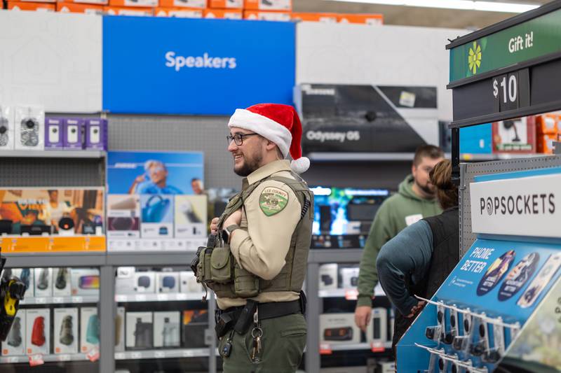 Lee County officer Alejandro Castro laughs as he waits in line with his shopper during Shop with a Cop on Saturday, December 14th, 2024. Kids could grab a cookie, do some coloring and get a photo with Santa after finishing up their shopping.