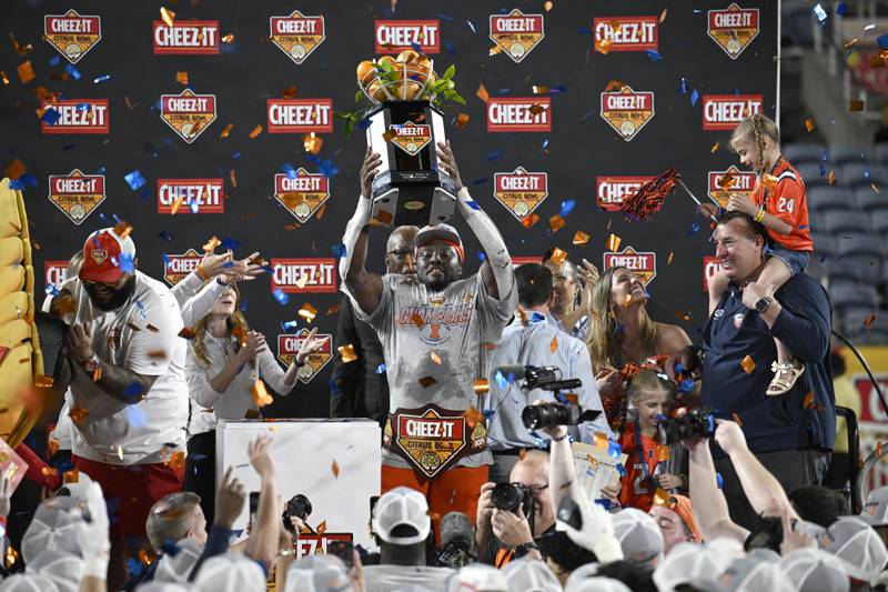 Illinois running back Josh McCray, center, raises the championship trophy after his team's win over South Carolina in the Citrus Bowl NCAA college football game as head coach Bret Bielema, right, looks on, Tuesday, Dec. 31, 2024, in Orlando, Fla. (AP Photo/Phelan M. Ebenhack)