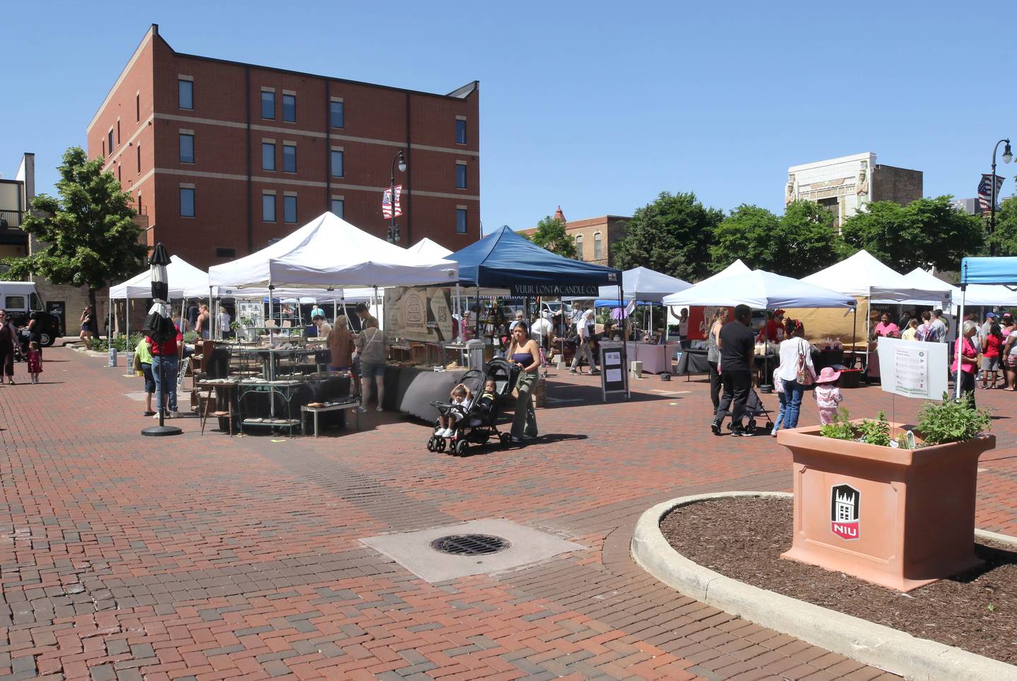 Attendees visit the tents during a very windy opening day at the DeKalb Farmers Market Thursday, June 6, 2024, at Van Buer Plaza in Downtown DeKalb. The market will run from 10 a.m. to 2 p.m. Thursdays through Sept. 19.