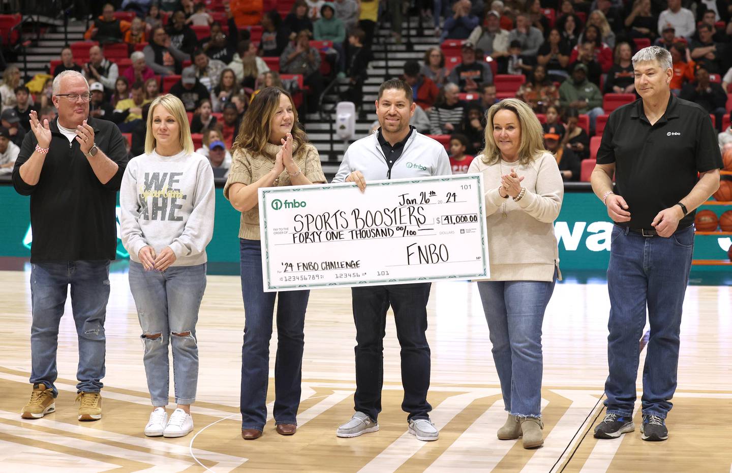 DeKalb and Sycamore boosters and staff along with members of FNBO pass a check Friday, Jan. 26, 2024, for $41 thousand dollars that was collected for this years event during the FNBO Challenge in the Convocation Center at Northern Illinois University.