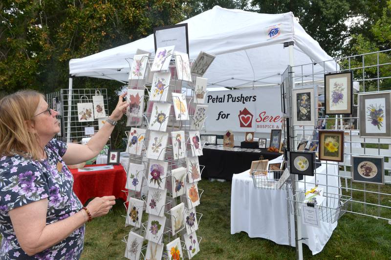 Carolyn McBride, a volunteer for Serenity Hospice and Home, adjusts some of the "Petal Pushers" items for sale at the 74th Grand Detour Arts Festival held on Sunday, Sept. 10, 2023 at the John Deere Historic Site in Grand Detour.