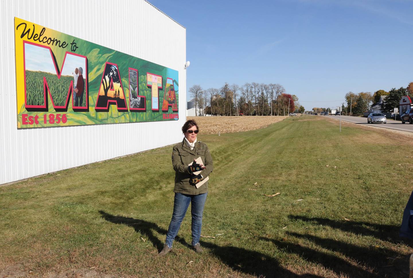 Jacque Fucilla, a member of the Malta Seedling Committee, talks about the new mural by Dixon artist Nora Balayti before the official ribbon cutting Wednesday, Oct. 19, 2022, on the north side of Route 38 in Malta. The mural, which spells out Malta in large capital letters, depicts the values of the town with themes of agriculture, family, community and growth.