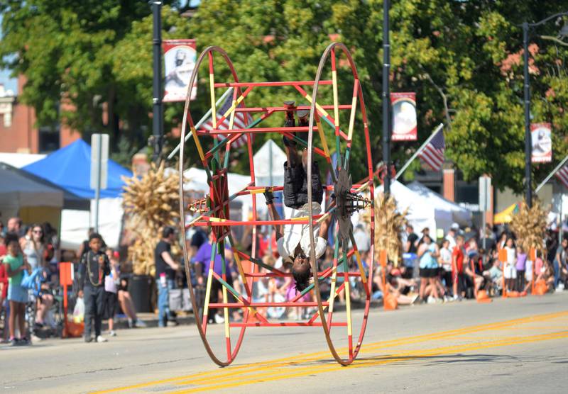 A paid performer is upside down as he rides a big wheel in the Harvest Time Parade during the Autumn on Parade festival on Sunday, Oct. 5, 2025 in Oregon.