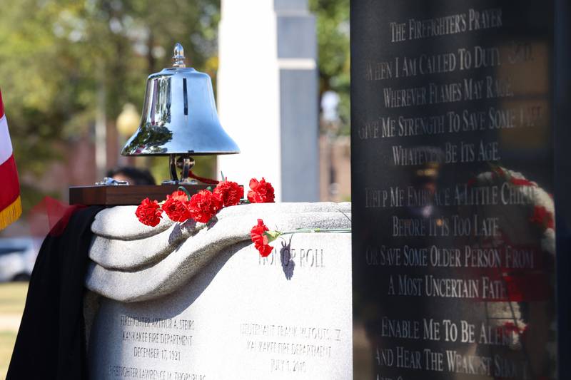 Flowers rest upon the memorial wall as a firefighter's reflection is seen on the engraved prayer during the 44th Kankakee County Fallen Firefighter Memorial Service on Friday, Oct. 3, 2025.
