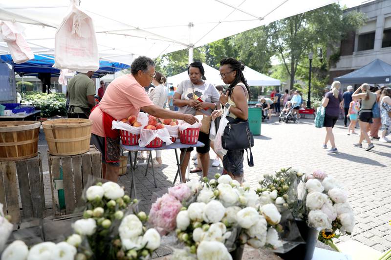 Mona Moore (left) sells peaches to Shirley Knight (center) and Cathy Washington (right) during the weekly farmer’s market in La Grange on Thursday, July 20, 2023.