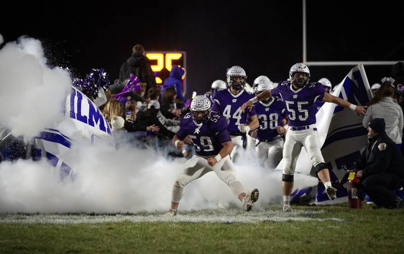 Wilmington's Zach Ohlund, center, Logan Van Duyne, right, and Declan Moran, center background, charge onto the field with their team before the start of the Class 2A semifinal against El Paso-Gridley on Saturday, November 22, 2025.