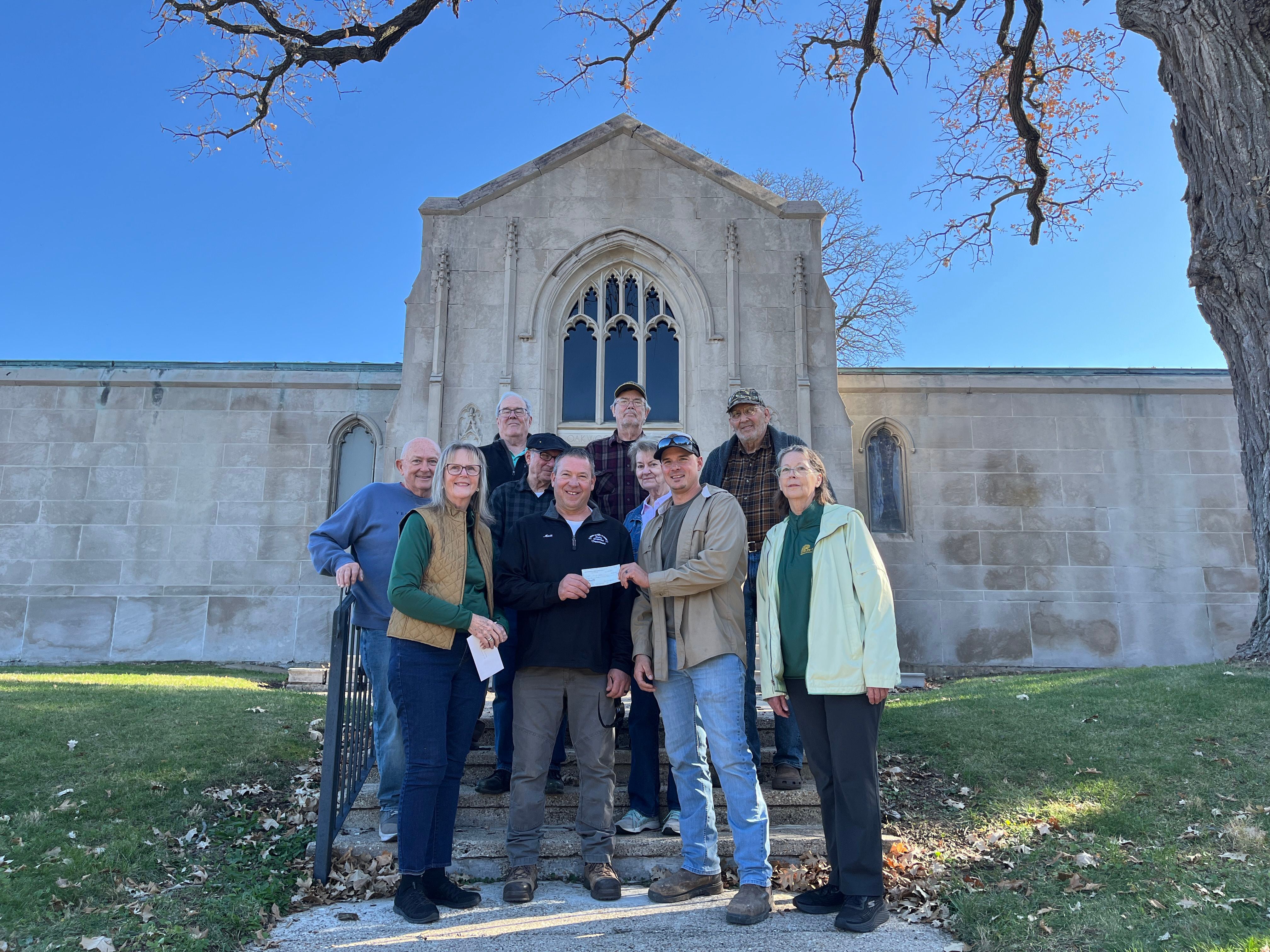 The Lee County Historical Society donated $1,000 to the city of Dixon Nov. 14, 2025, for Oakwood Cemetery Mausoleum restorations. Pictured (front row) historical society members Jan Conkrite (left) and Rena Burgess (right), Dixon Street Department Manager Tyler Venier (middle right) and Oakwood Cemetery Foreman Matt Muller (middle left). Also pictured are historical society members (second row, from left) Gary Michel, Dave Wyman, Joan Janssen, (third row, from left) Mike McBride, Gary Janssen and Gary Burgess. 