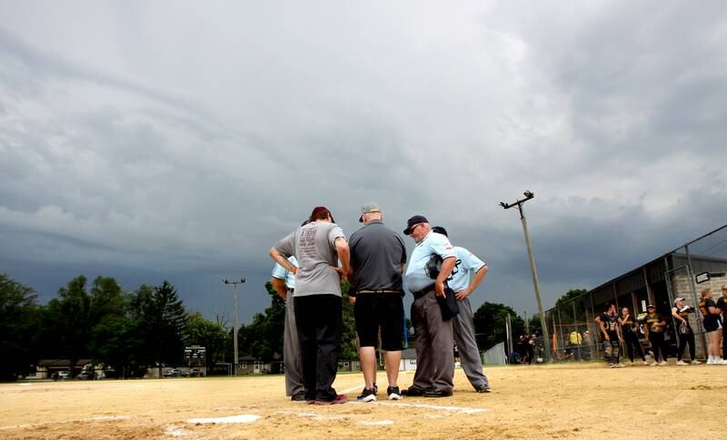 Umpires and coaches meet at home plate to discuss the weather as a storm rolls in for Prairie Ridge and Harvard’s game in Class 3A softball regional final action at Lions Park in Harvard Friday.