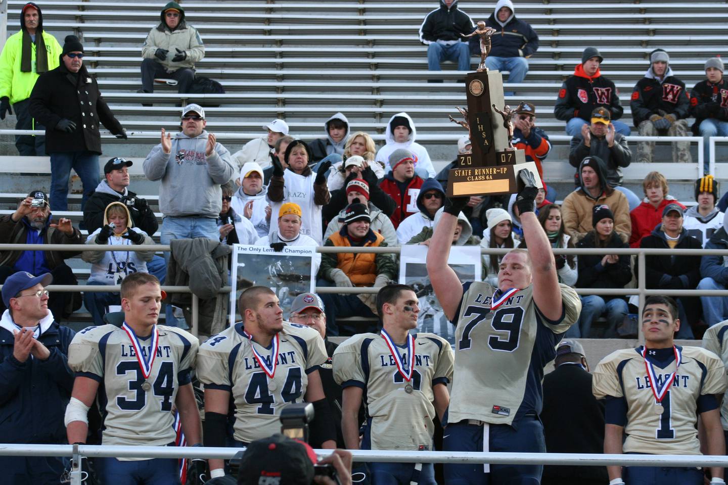 Graham Pocic (79) holds the 2007 Class 6A state runner-up trophy as teammate Willie Hayes (44) looks on. Pocic and Hayes, once teammates, are now together again as coaches on the Lemont coaching staff as Hayes takes the reins as head coach.