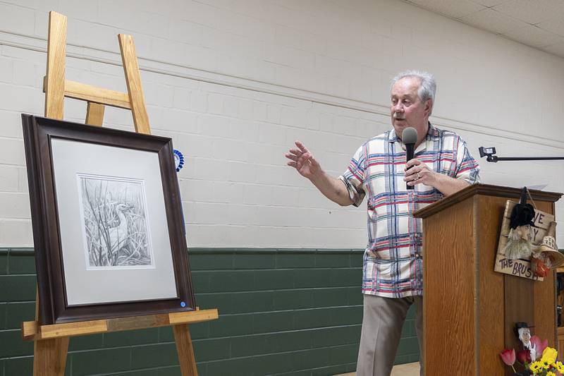 Larry K. Johnson of Geneva presents a work by Carolyn McKee Freese Thursday, April 16, 2026, as the judge of the 77th Phidian Art Show in Dixon. McKee Freese was awarded the Ann Roe Memorial Award.