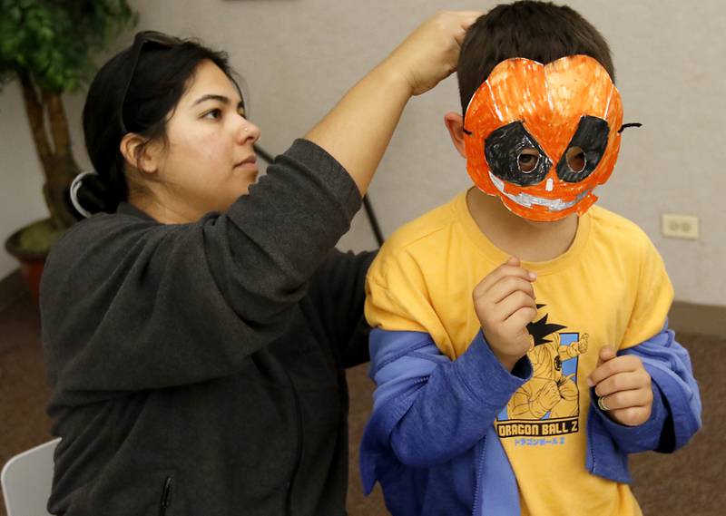Rosa Gonzalez putts the mask her son, James, Lunak, 6, made on his face as children make masks on Wednesday, Oct. 23, 2024, during at Kids Crafternoon at the Harvard Diggins Library. Children were able to chose between several Halloween themed masks to make.