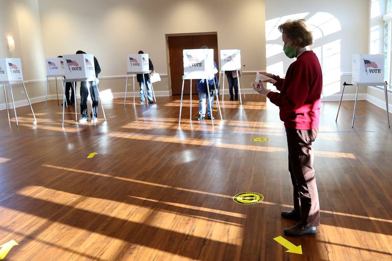 Election judge Vicki Ridges, right, waits for voters to complete their ballots so she can wipe down the booths with a sanitizing wipe on Tuesday, Nov. 3, 2020 at Main Beach in Crystal Lake.