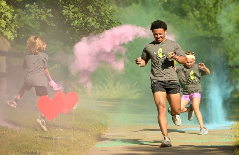 Dill Dash runners get doused with colorful powder along the race route during the Inaugural Pickle Paradise event at Pottawatomie Park in St. Charles on Friday, June 21, 2024.