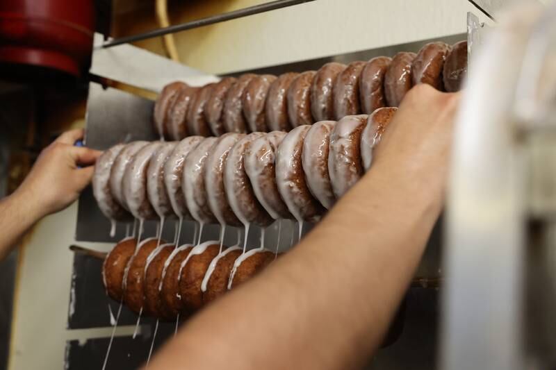 Diego Maldonado hangs freshly glazed cake donuts on a rack at Home Cut Donuts on Jefferson Street, Saturday, March 25, 2023 in Joliet.