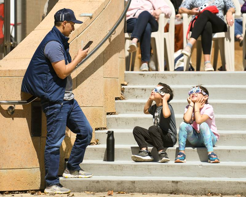 Gabriel Montalvo takes a photo of his kids Julian Montalvo,5, and Cataleya Montalvo, 6, of Aurora during the solar eclipse vewing party at the Wheaton library on Monday April 8, 2024.