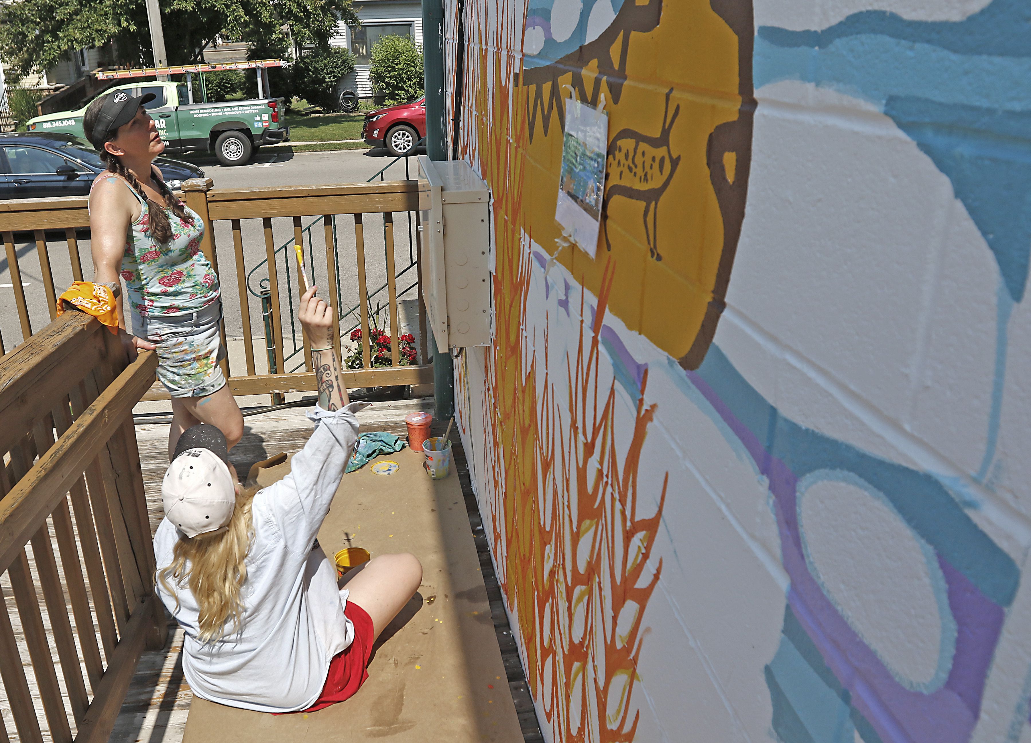 Jenny Mathews (standing) and Melinda Cook discus how the color looks as they paint a mural on Thursday, June 19, 2025, on the side of the McHenry Brewing Co., in McHenry. This is one of two new McHenry murals in McHenry. 