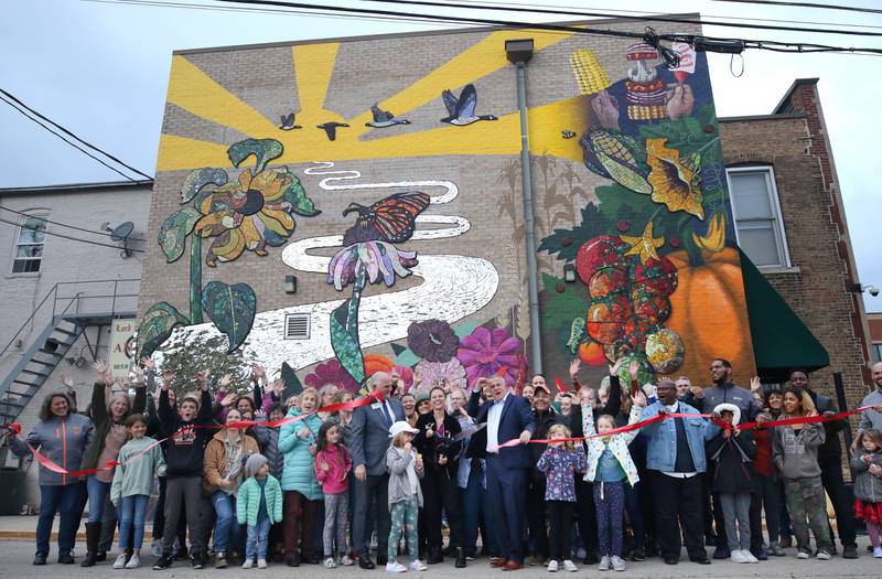 Mural artist Danielle Casali cuts the ribbon Thursday, Oct. 19, 2023, alongside city officials and some of the many volunteers who helped with the project during the unveiling and ribbon cutting of the new City Hall mural. The mural is on the on the south wall of City Hall.