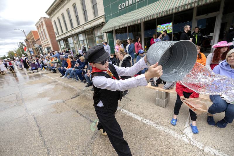 A youngster tosses a bucket of water onto the streets of Fulton Saturday, May 3, 2025, as the traditional cleaning of the parade route takes place during Fulton’s Dutch Days.