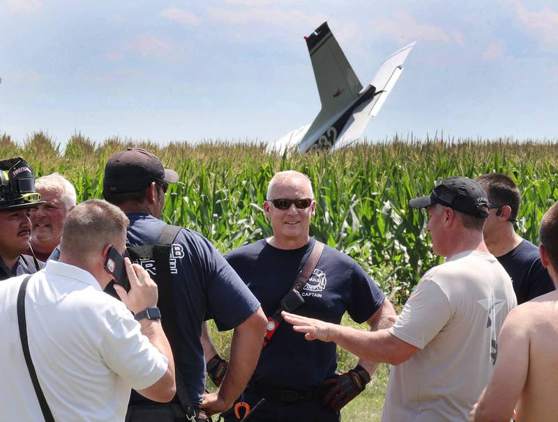 First responders talk as the tail section of a crashed plane protrudes from a cornfield Thursday, July 27, 2023, behind a business at 260 West Lincoln Highway in Cortland.