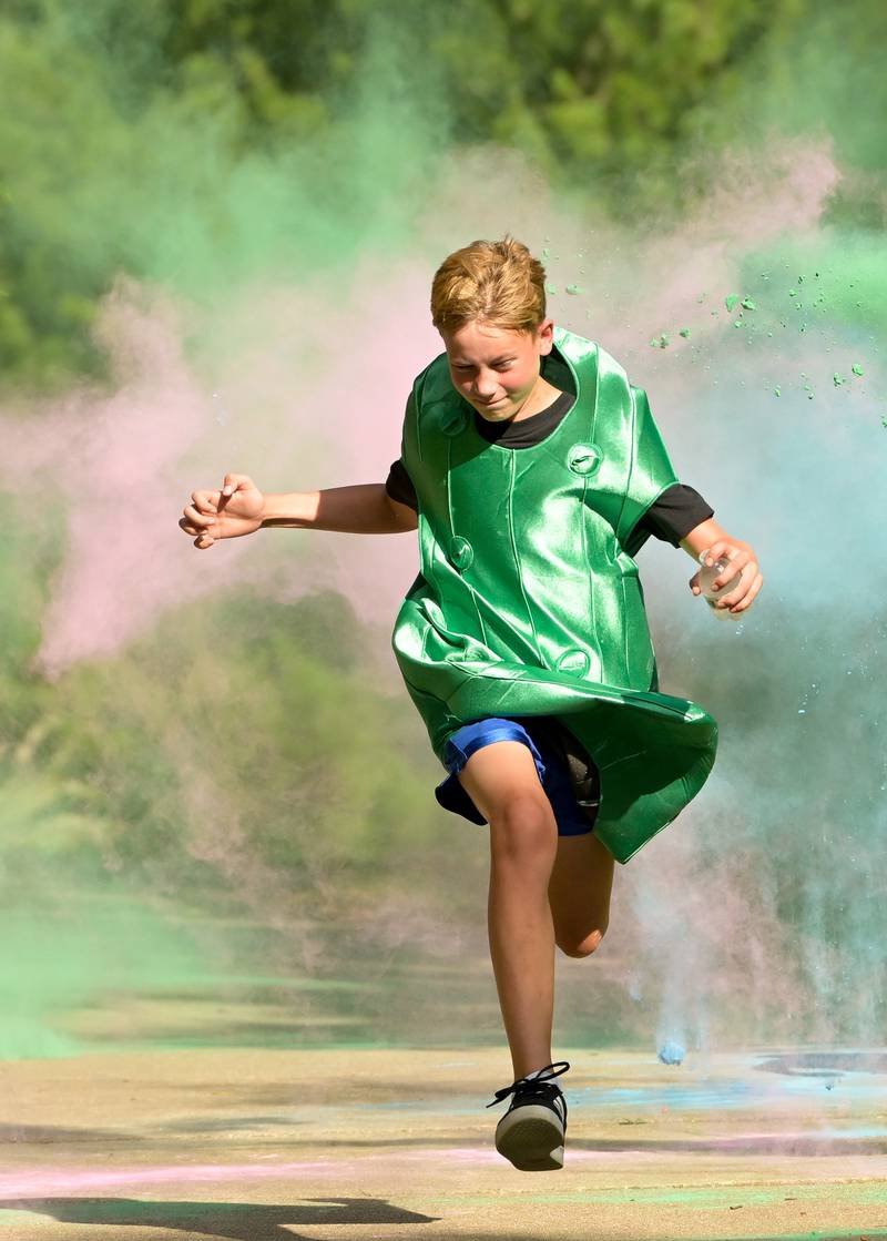 A pickle costumed Dill Dash runner gets doused with colorful powder along the race route during the Inaugural Pickle Paradise event at Pottawatomie Park in St. Charles on Friday, June 21, 2024.
