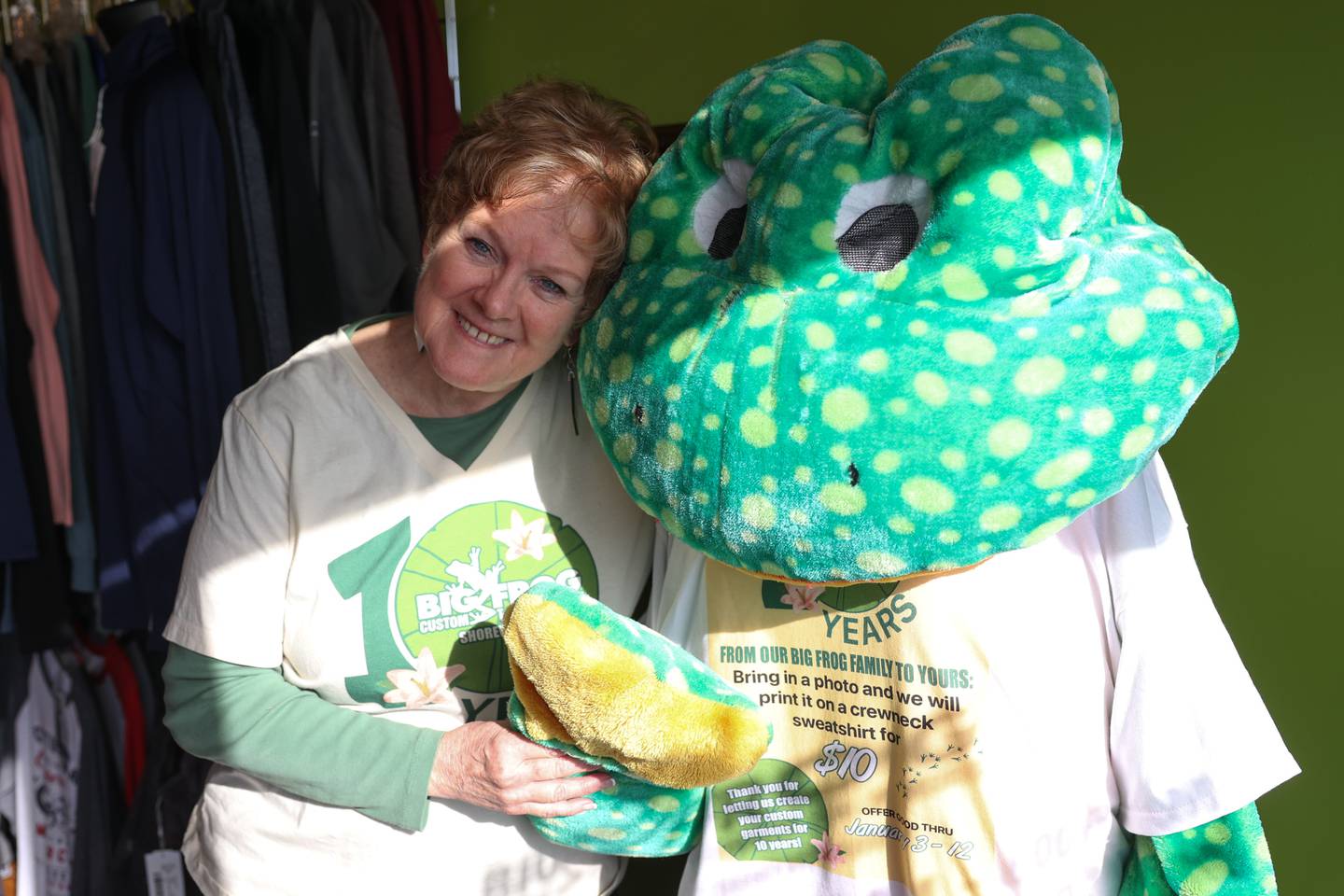 Shorewood’s Big Frog Custom T-Shirts & More owner Gail Girard stands with the store mascot that croaks when one passes by.