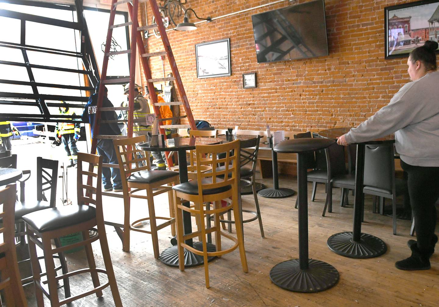 Katie Gatton, an employee at the Ogle County Bewery, moves a table as firefighters figure out how to safely remove the damaged garage door after a vehicle crashed into the business early Sunday afternoon.