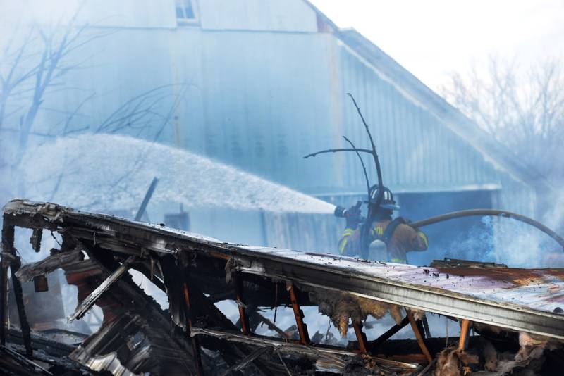 A firefighter hoses down a garage at 6727 W. Henry Road, southeast of Polo, on Wednesday, March 26, 2025. Several departments responded to the fire at the rural residence. A camper and at least one other vehicle in addition to other items inside and around the garage were destroyed in the blaze. No injuries were reported.