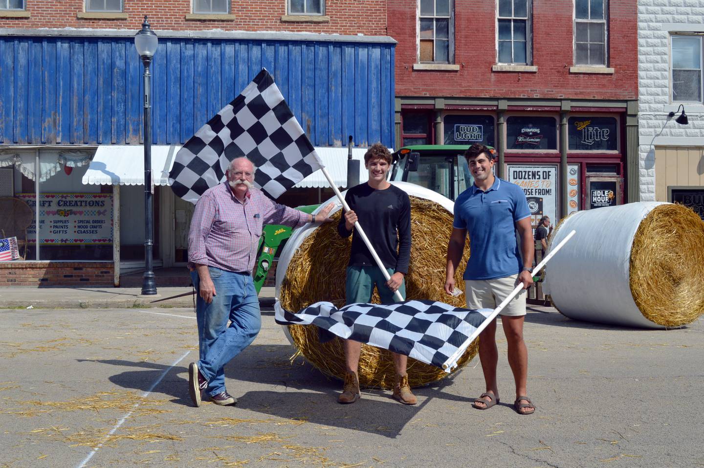 Tyler Willman, right and Levi Schuler, center both of Pine Creek, pose with U.S. National Straw Sculpting Competition organizer Jeff Bold in front of a 700-pound straw bale on Aug. 27 during StrawFest Day. Willman and Schuler won the races by rolling the bale 75 feet in 10.08 seconds.