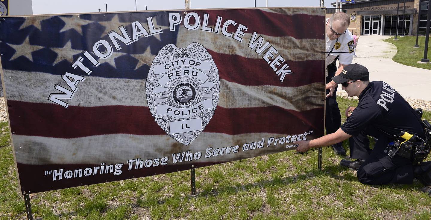 Peru Police Chief Robert Pyszka and Patrolman Nick Biagioni attach the banner for National Police Week on Friday, May 13, 2022, outside the Peru Police Department. Five of the banners will be posted throughout Peru. Banners were donated by MCS Advertising in Peru.