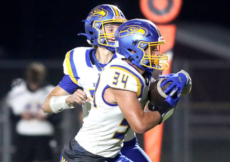 Johnsburg’s Duke Mays, front, grabs a handoff from Carter Block in varsity football at Rod Poppe Field on the campus of Marengo High School in Marengo on Friday, Oct. 3, 2025.