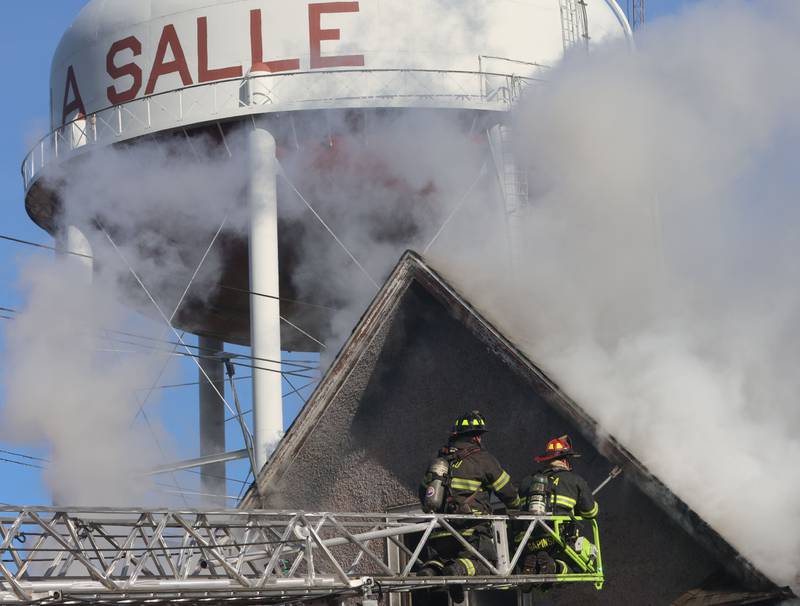 Firefighters position the Peru aerial ladder truck at the top of the attic of a burning structure fire as the La Salle water tower is visible overhead in the 800 block of Bucklin Street on Friday, Jan. 23, 2026 in La Salle.