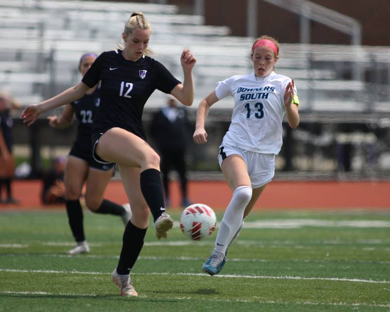 Downers Grove North's Ava Locker (12) kicks the ball while being defended by Downers Grove South's Emily Petring (13) during soccer match between Downers Grove North at Downers Grove South.  May 6, 2023.