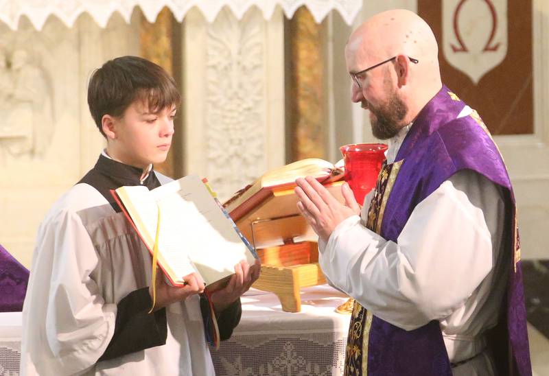 James Arkins a student at Trinity Catholic Academy, holds the lectionary for opening prayer for The Very Rev. Father Tom Otto during Ash Wednesday on Wednesday, March 5, 2025 at the Queen of the Holy Rosary Church in La Salle.
