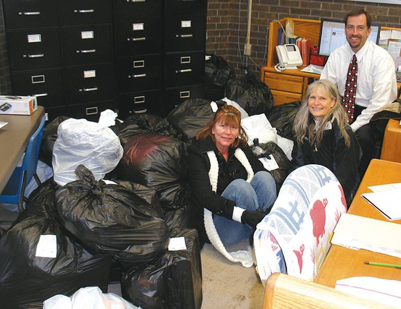 Oregon Rotary Club members Sue Miatke and Mary Jo Griffin and Etnyre Wing Principal Mike Lawton sit among the bags of winter gear collected in December for Keeping Kids Warm project. Photo supplied