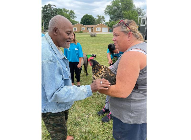 Lisa Afshari, founder of Ready Set Ride in Plainfield (right), holds out a therapy chicken so Melvin, a client at United Cerebral Palsy-Center for Disability Services in Joliet, can interact with it.