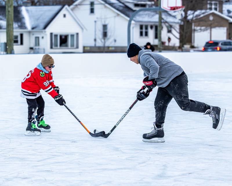 Weston Harris and Timmy Dierks fight over possession of puck whilst iceskating during game of hockey at Schweickert Arena's Ice Rink on Tuesday, December 30, 2025, at Washington Park in Peru.