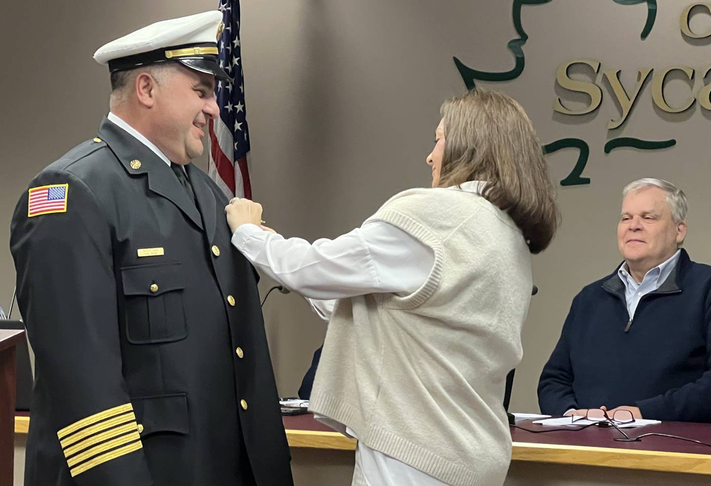 Sycamore Mayor, Steve Braser, right, watches as Kelly Reina, middle, pins the Sycamore fire chief badge to her husband on Jan. 18, 2023, when Carl Reina was sworn-in as the Sycamore fire chief.