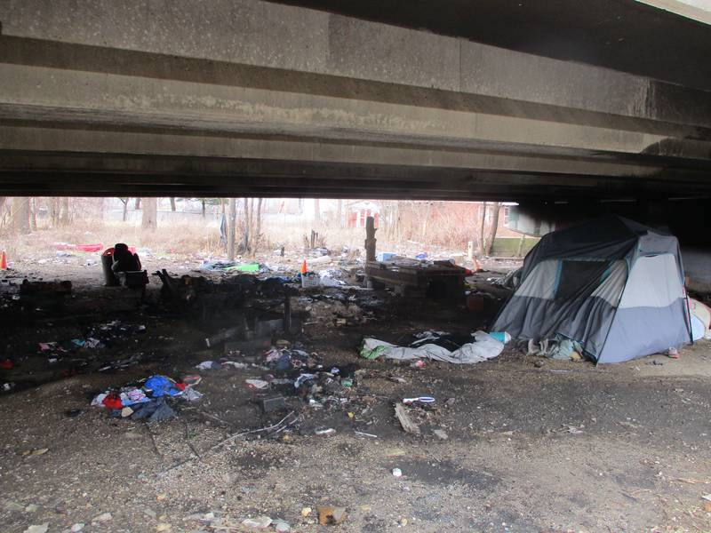 The charred ground from a tent fire under a Cass Street bridge in Joliet Township lie next to a tent on the site on Saturday, March 4, 2023.