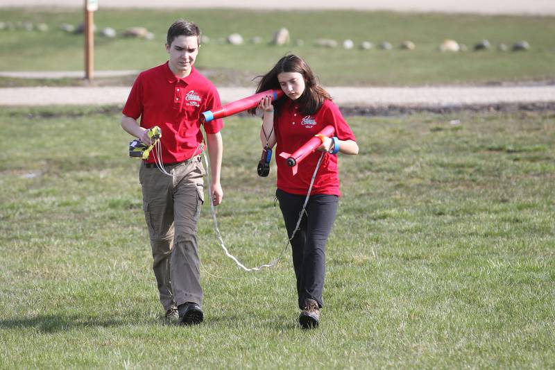 Luka Weideman, of Lindenhurst walks with Lilly Abney, of Round Lake Beach, both 14, with the Prince of Peace Redhawk Rocketeers TARC Team, as she listens to the electronics beep out the altitude using an altimeter in their rocket after retrieving it from a field after test launching it to compete in the upcoming American Rocketry Challenge at the Tim Osmond Sports Complex in Antioch.