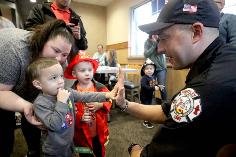 Firefighter Brad DeRaedt, right, is greeted by Emmett Irazoque, 2, left, of Lake in the Hills, and his mom, Alexis, during a Read & Eat Fries With a Firefighter event Thursday, March 16, 2023, at the Culver’s in Huntley. At center is Rhett Millard, 3, of Lake in the Hills.